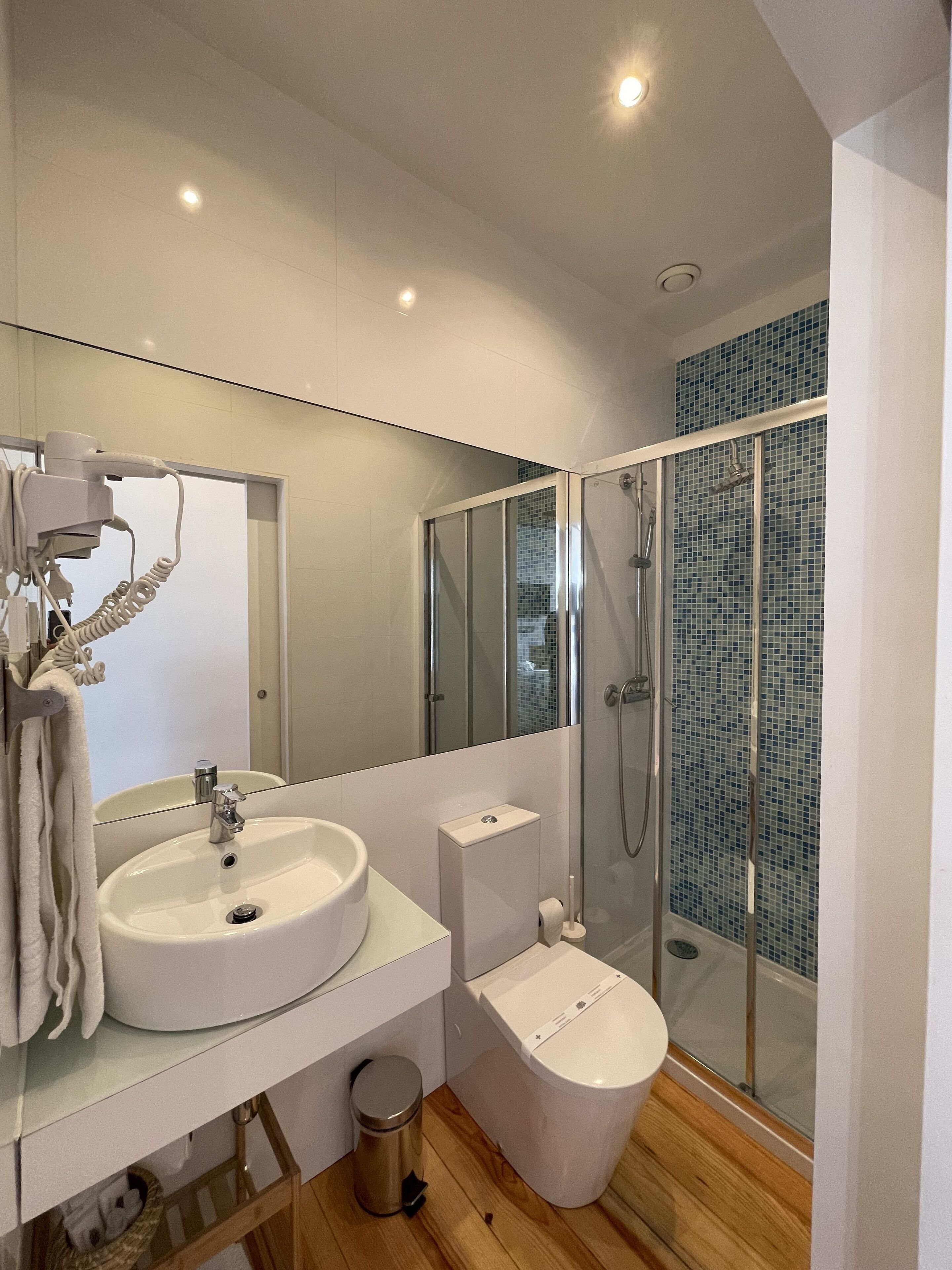 A modern bathroom with a white sink, mirror, and glass-enclosed shower.
