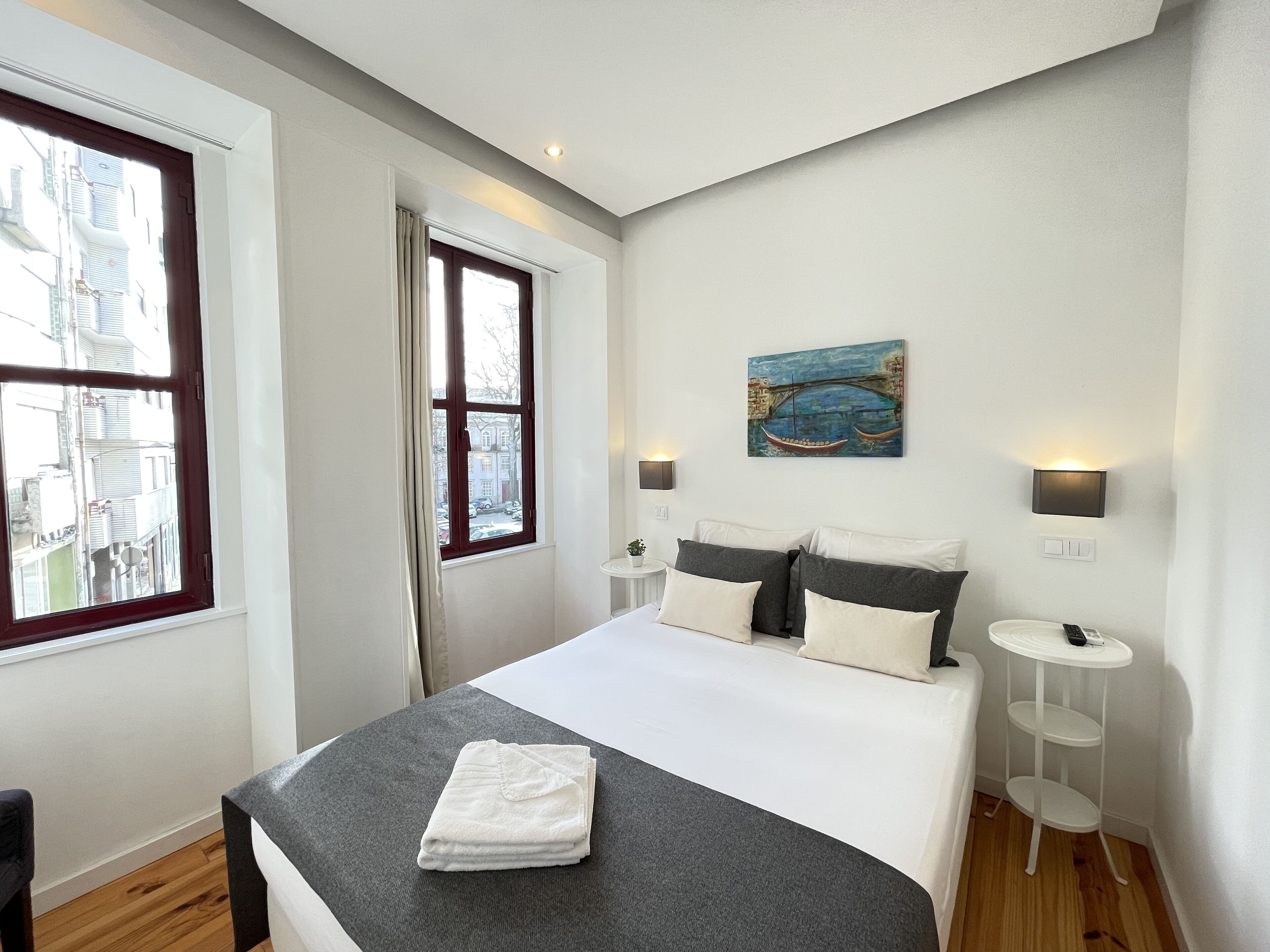 Een slaapkamer met een bed, een raam, een schilderij, nachtkastjes en een nachtkastje.