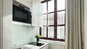 Et kompakt køkken med indbygget mikrobølgeovn, vask og et vindue med gardiner.