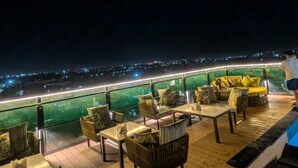A night-time outdoor seating area with tables and chairs, overlooking a cityscape. - Red Fox by Lemon Tree Hotels, Alwar (Alwar)