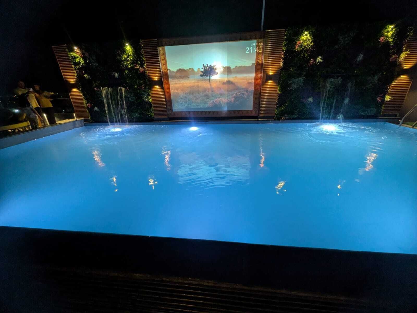 Una piscina con chorros de agua, rodeada por una terraza de madera y follaje.