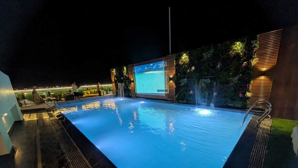 A nighttime swimming pool with a waterfall feature, a large screen, and a well-lit outdoor seating area. - Red Fox by Lemon Tree Hotels, Alwar (Alwar)