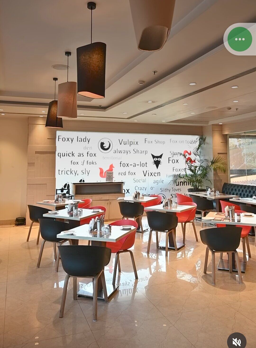 A modern dining area with tables and chairs, a large wall with various text and logos, and pendant lighting.