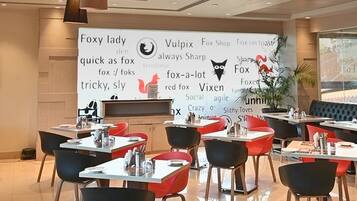 A modern dining area with tables and chairs, a large wall with various text and logos, and pendant lighting.