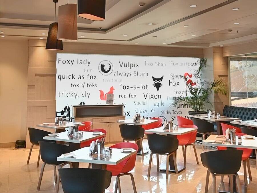A modern dining area with tables and chairs, a large wall with various text and logos, and pendant lighting.