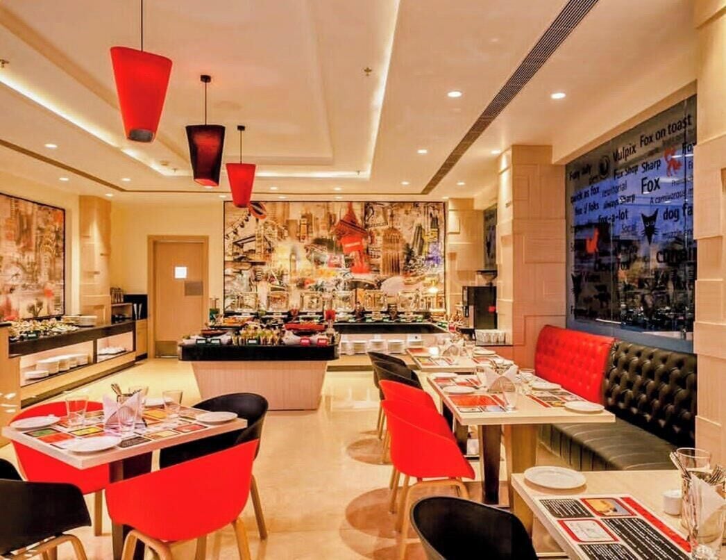 Un restaurante con varias mesas y sillas, una zona de bar y una sección de asientos con un banco tapizado rojo.