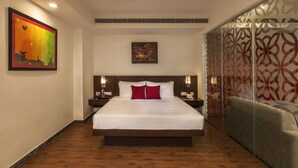 A hotel room with a large bed, a nightstand, a bedside table, a wall-mounted painting, and a patterned curtain. - Red Fox by Lemon Tree Hotels, Alwar (Alwar)