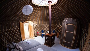 A cozy yurt interior with two beds, a wooden cabinet, a small table, and a fire pit. - Raet Camping (Arendal)