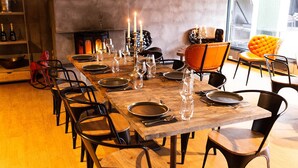 A long dining table set with plates, glasses, and candles, surrounded by black chairs in a room with a fireplace and a large window. - Raet Camping (Arendal)