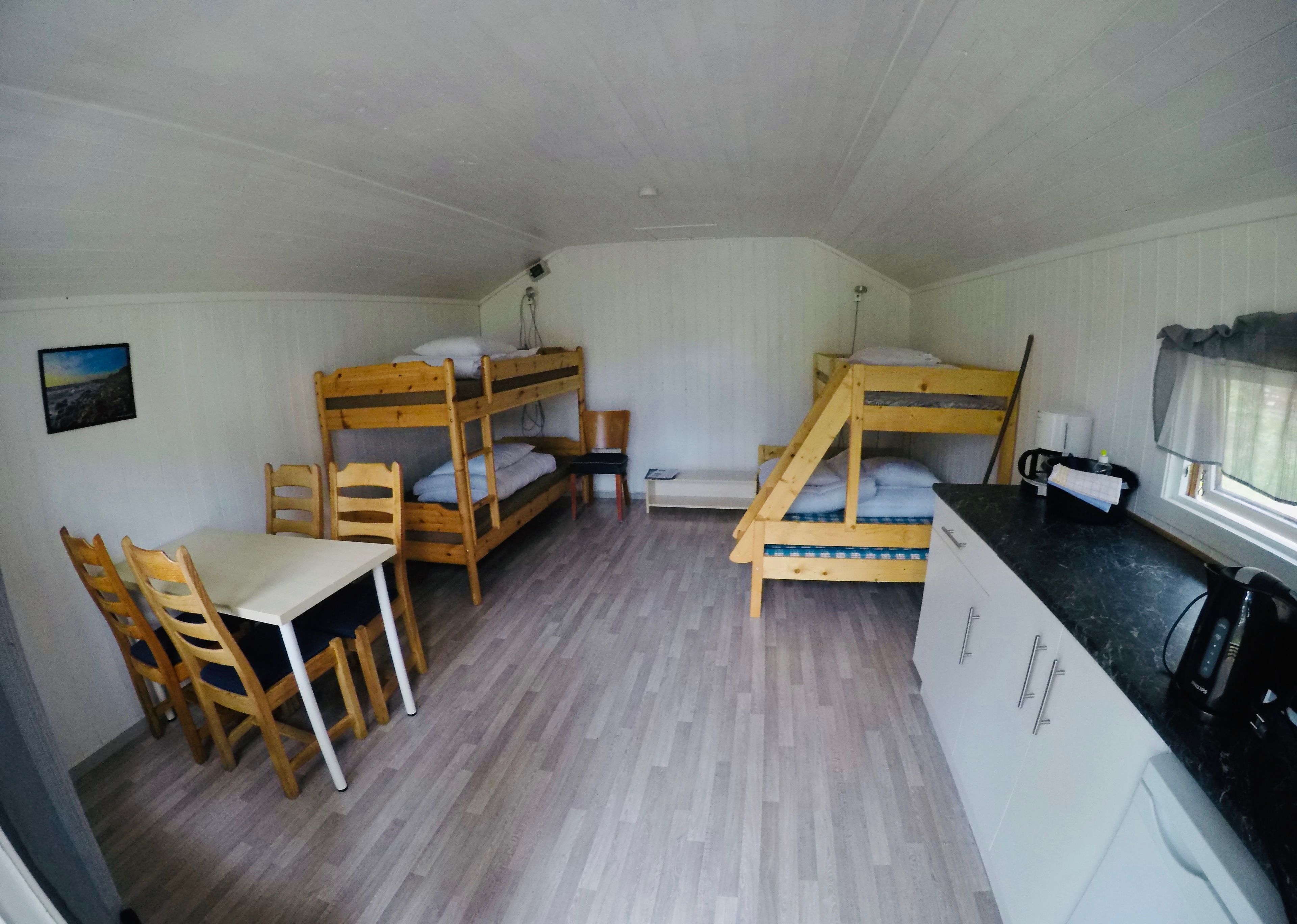 A compact room with bunk beds, a small table with chairs, a kitchenette, and a window with curtains.