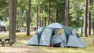 A camping tent in a wooded area with a picnic table nearby.