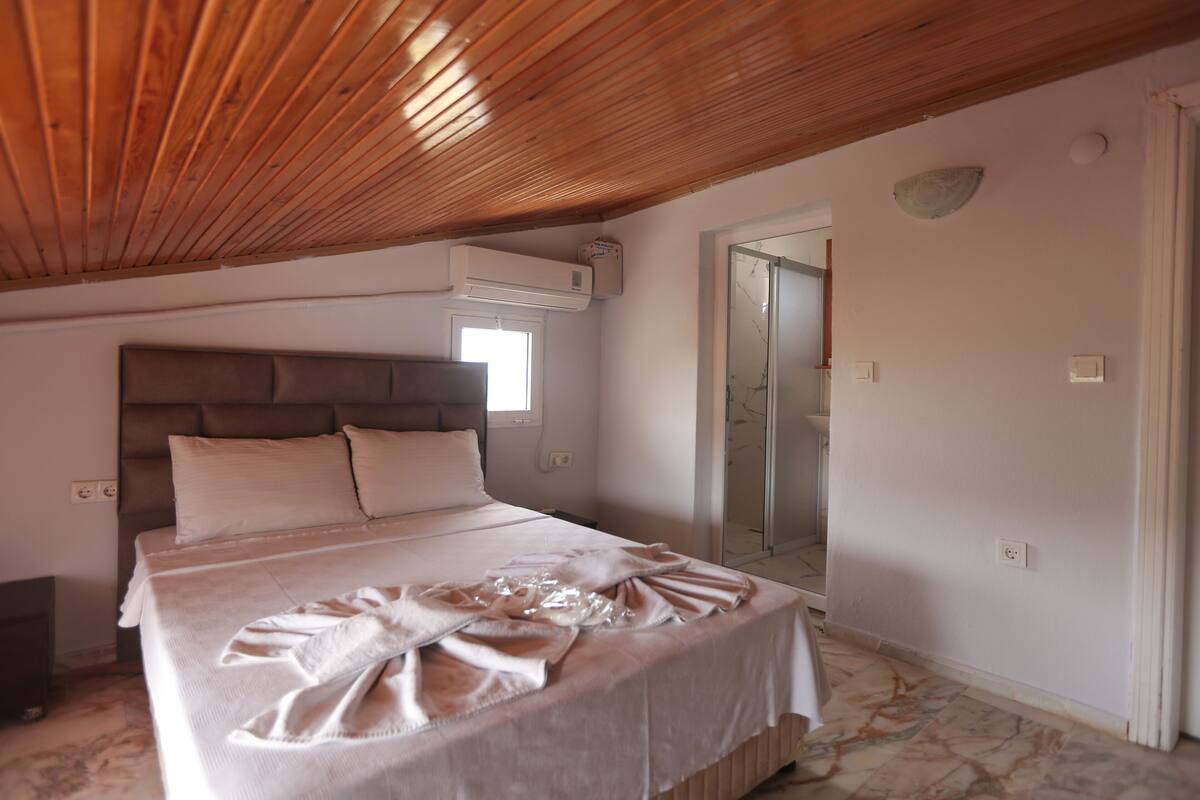 Ein Schlafzimmer mit Holzboden, einem großen Bett mit Kopfteil, einem Fenster und einem Spiegel an der Wand.
