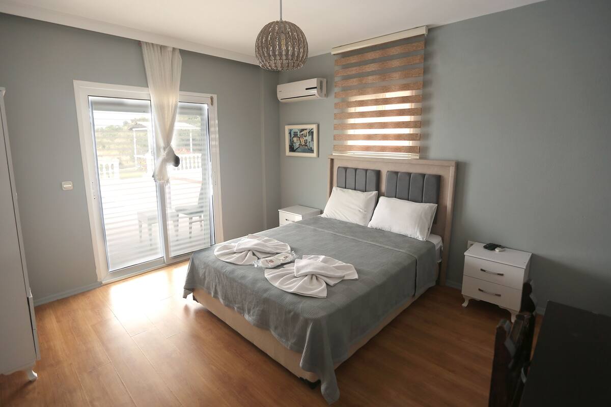 Ein Schlafzimmer mit einem Bett, einem Nachttisch, einer Kommode, einem Fenster mit Jalousien und einer Deckenleuchte.