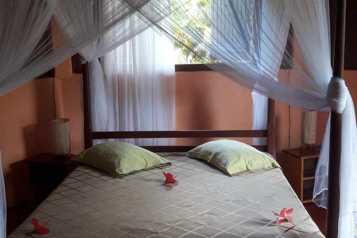 A bed with a canopy, green pillows, and a quilted bedspread.