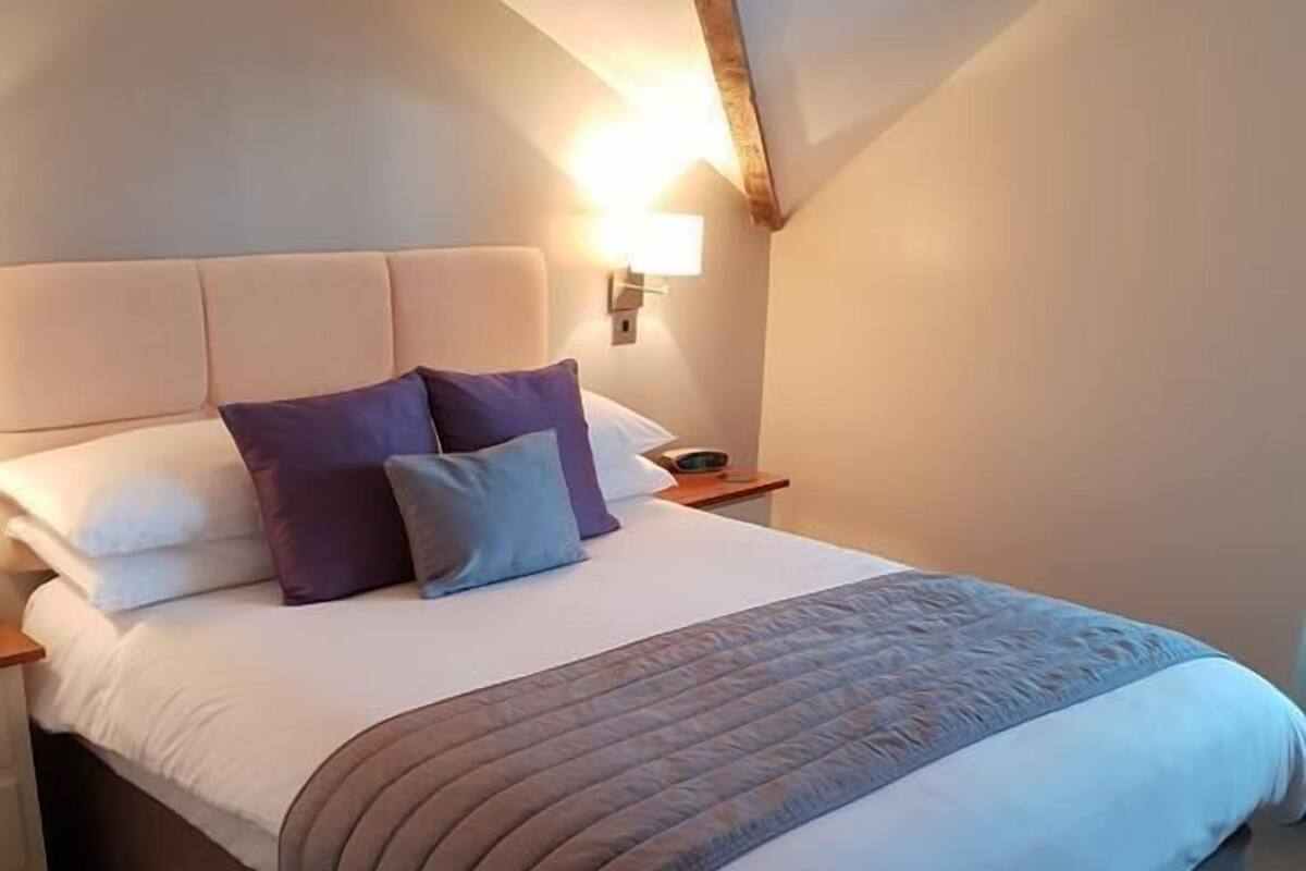 Ein Schlafzimmer mit einem großen Bett, einem Kopfteil, Nachttischen und einer Wandleuchte.