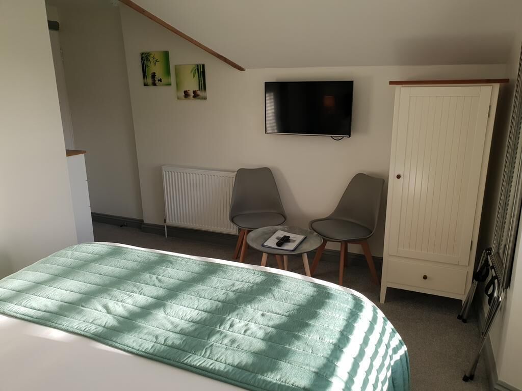 Une chambre à coucher avec un lit, un téléviseur fixé au mur, deux chaises et un radiateur.
