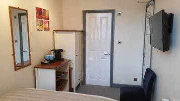 Habitación de hotel con cama, escritorio con cafetera, silla, televisor montado en la pared y una puerta.