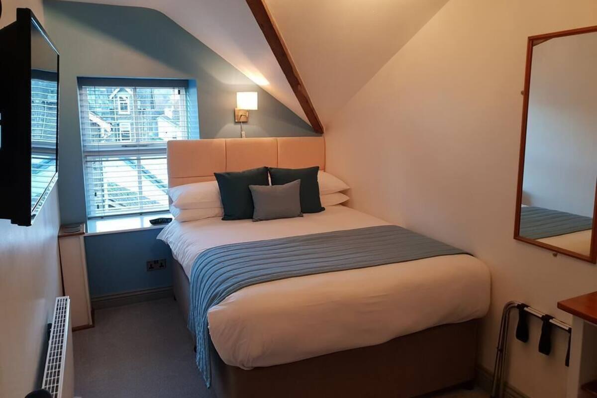 Ein Schlafzimmer mit einem Bett, einem Fenster, einem Nachttisch und einem Spiegel.