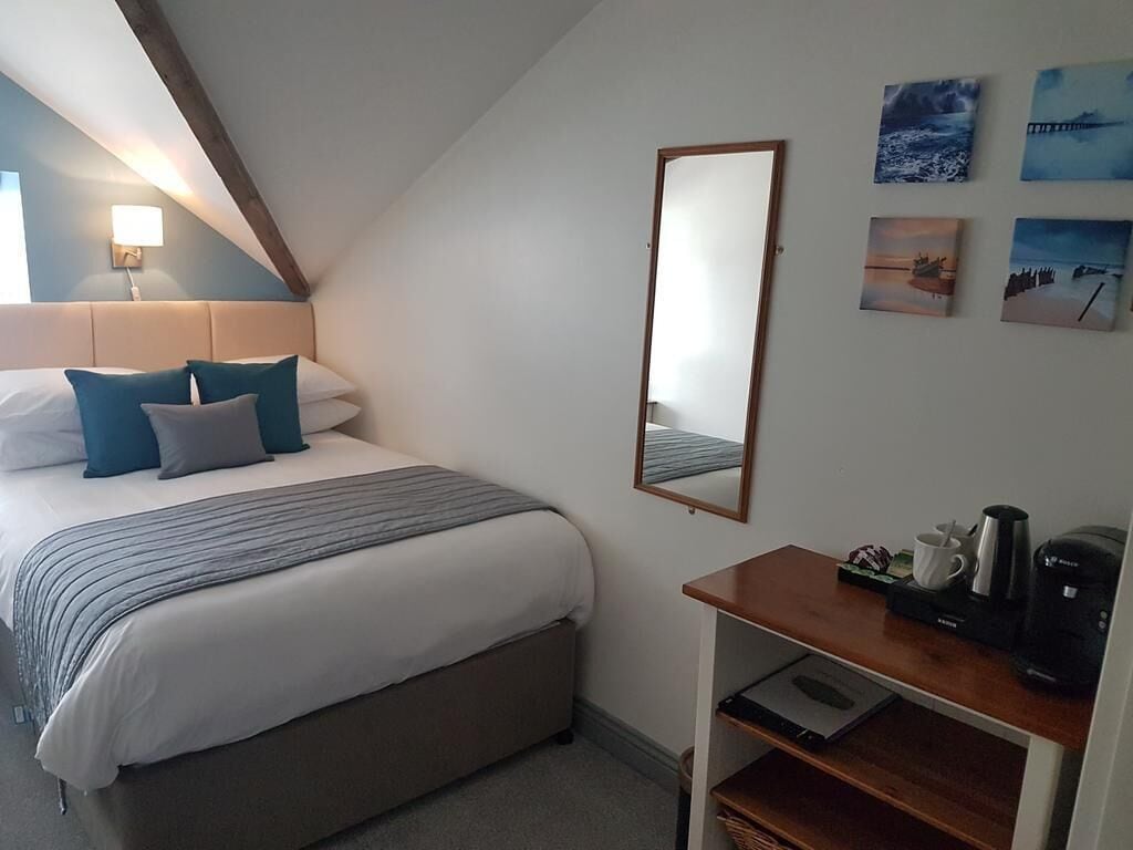 A bedroom with a bed, a bedside table with a coffee maker, a mirror, and artwork on the wall.