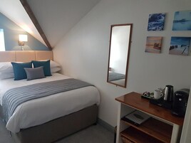 A bedroom with a bed, a bedside table with a coffee maker, a mirror, and artwork on the wall.