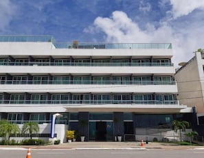 A modern multi-story building with a flat facade, large windows, and a covered entrance area with potted plants. - Flat Beira-Mar Nord Blue Sunset (João Pessoa)