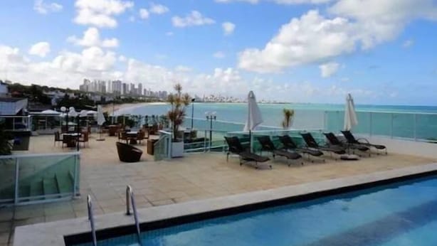 A poolside area with lounge chairs and umbrellas, overlooking a beach and ocean. - Flat Beira-Mar Nord Blue Sunset (João Pessoa)