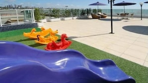 A playground with a blue slide and yellow and red ride-on toys on artificial grass. - Flat Beira-Mar Nord Blue Sunset (João Pessoa)