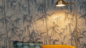 A yellow sofa with a patterned pillow, a floor lamp, and a wall with a bamboo wallpaper.
