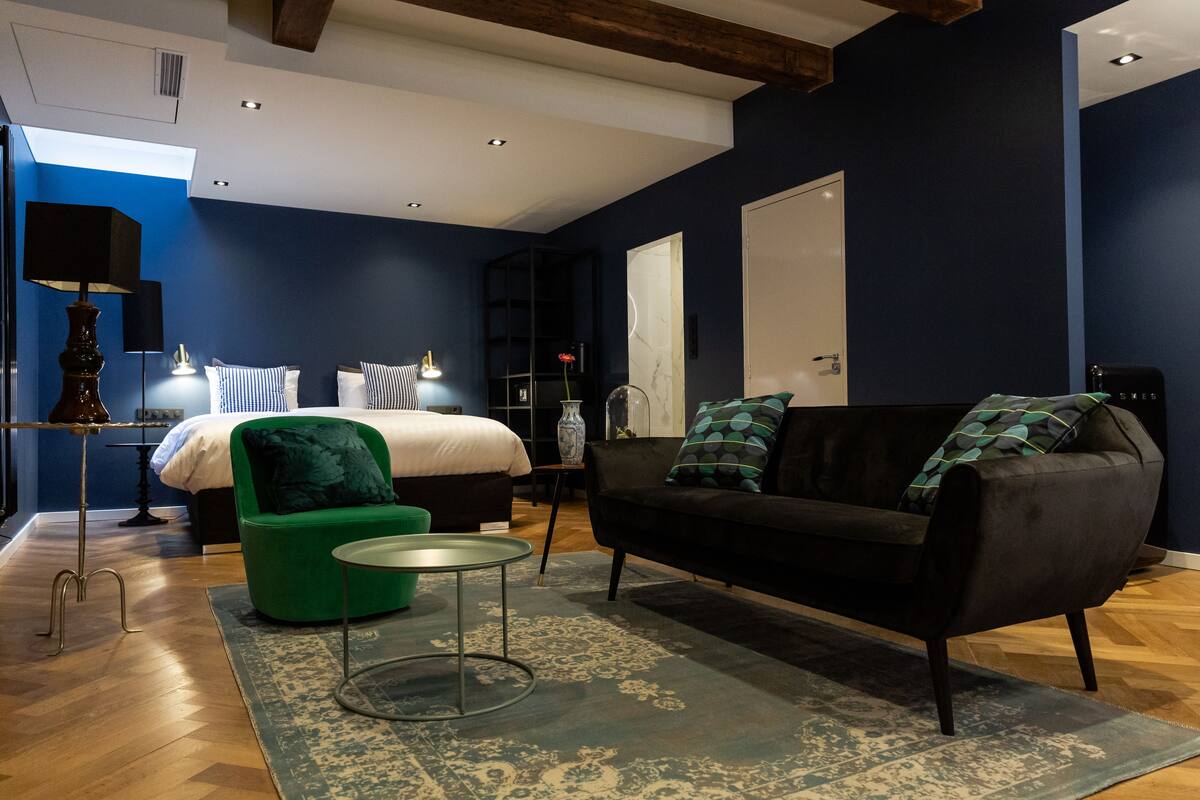 Une chambre à coucher moderne avec un lit, un fauteuil vert, un canapé noir et une petite table ronde.