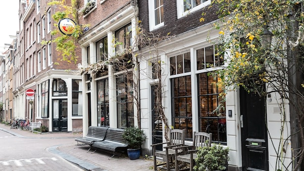 A row of traditional European buildings with large windows and a bench on the sidewalk.