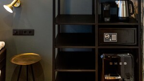 A modern room with a black shelving unit, a hanging light fixture, a coffee maker, and a compact refrigerator.