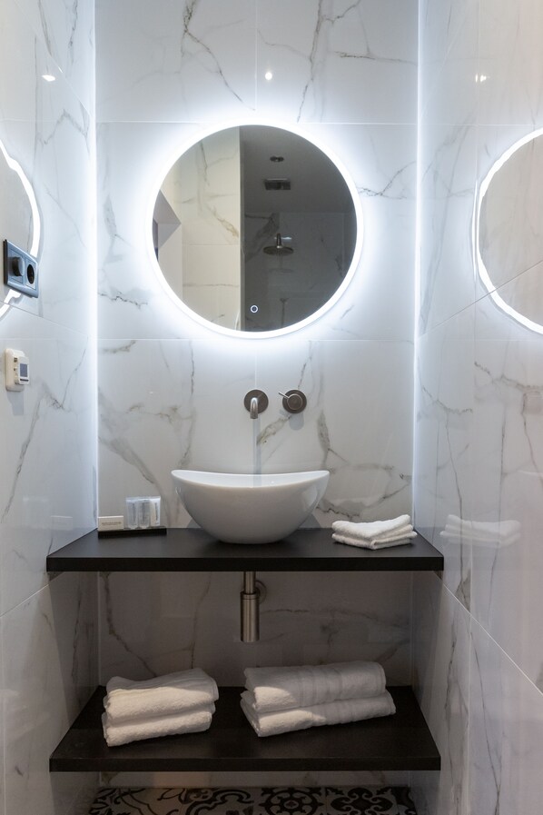 Un baño moderno con un lavamanos ovalado grande, un espejo redondo y un perchero.