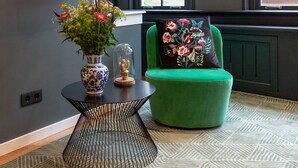 A modern living room with a green sofa, a black TV mounted on the wall, and a patterned rug.