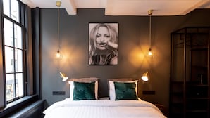 A bedroom with a large bed, two wall-mounted lights, a window, and a painting on the wall.