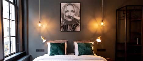 A bedroom with a large bed, two wall-mounted lights, a window, and a painting on the wall.
