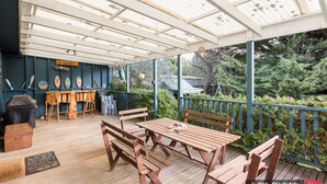A covered outdoor area with wooden benches and tables, a bar area with a counter and stools, and a view of greenery. - Heyley Haven, the perfect family getaway. (VENTNOR)