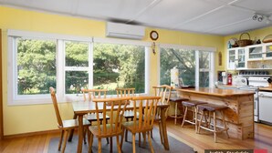 A kitchen with a large window, wooden chairs, a wooden table, and a kitchen counter with various items. - Heyley Haven, the perfect family getaway. (VENTNOR)