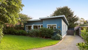 A single-story house with a blue exterior, a front yard with a well-maintained lawn, and a gravel driveway leading to the entrance. - Heyley Haven, the perfect family getaway. (VENTNOR)