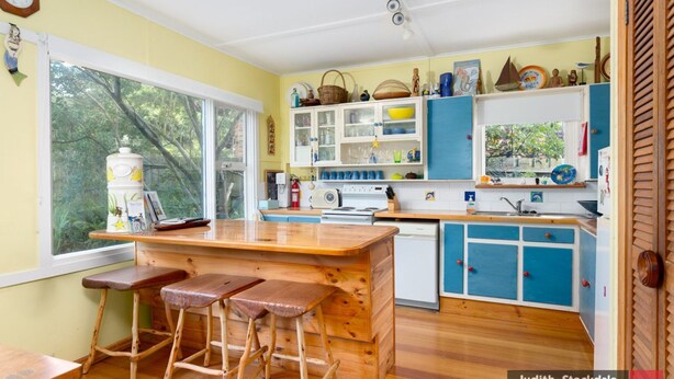 A kitchen with wooden stools, a stove, and a window overlooking greenery. - Heyley Haven, the perfect family getaway. (VENTNOR)