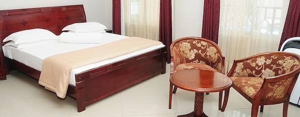 A hotel room with a bed, a bedside table, two chairs, and a window with curtains.