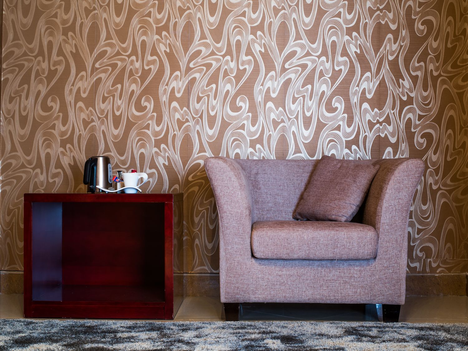Un salón moderno con un papel tapiz estampado, una mesita auxiliar roja con una cafetera y un sofá rosa.