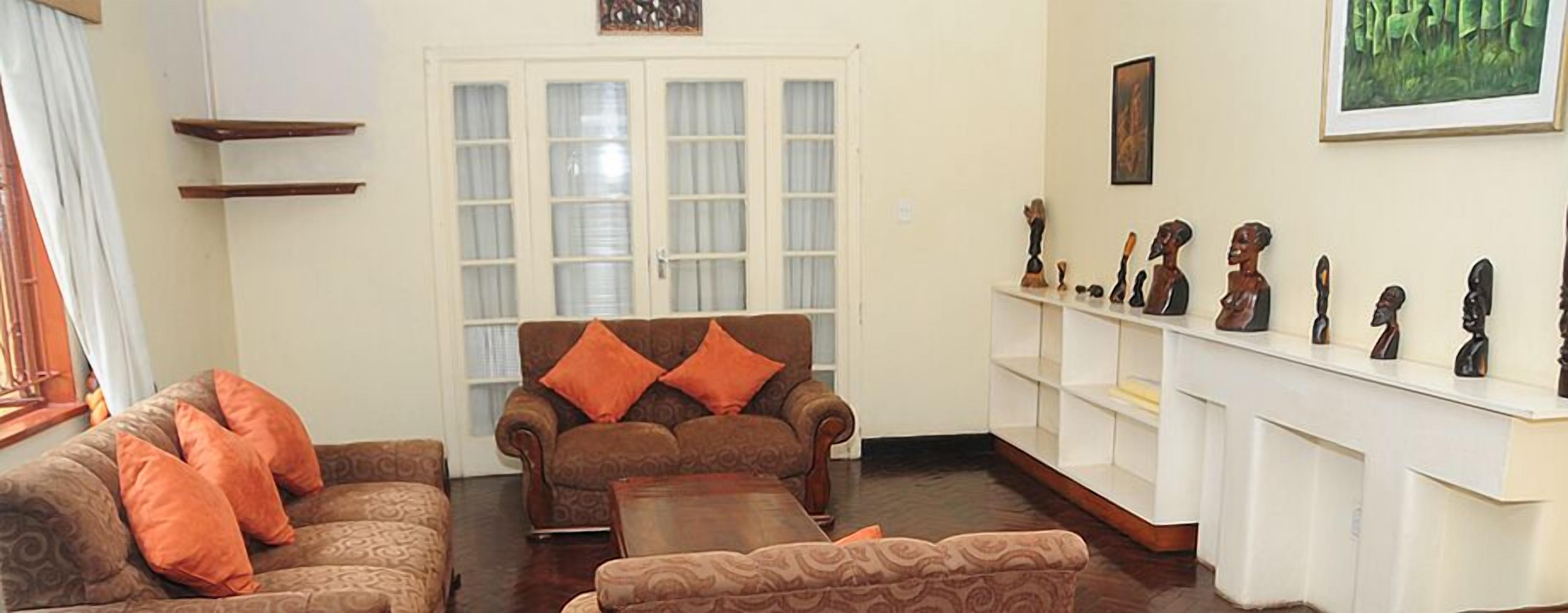 A living room with a brown sofa set, a coffee table, and a white shelving unit displaying wooden sculptures.