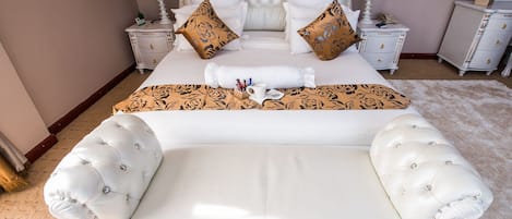 A spacious bedroom with a large bed, two nightstands, a dresser, and a chaise lounge.