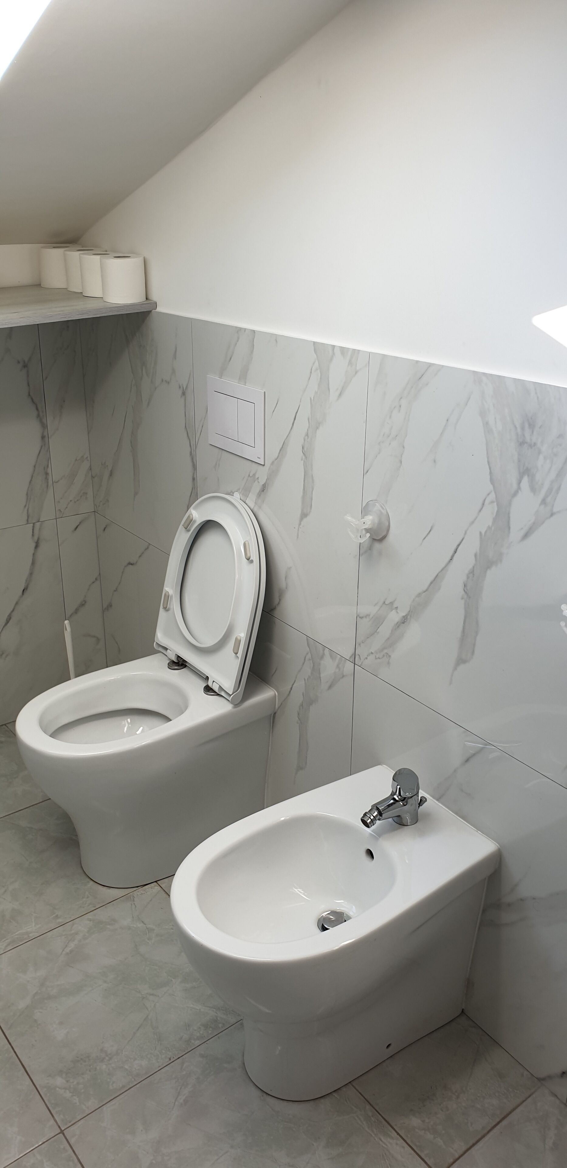 Une salle de bain avec des toilettes et un bidet, des murs en marbre et un luminaire au plafond.