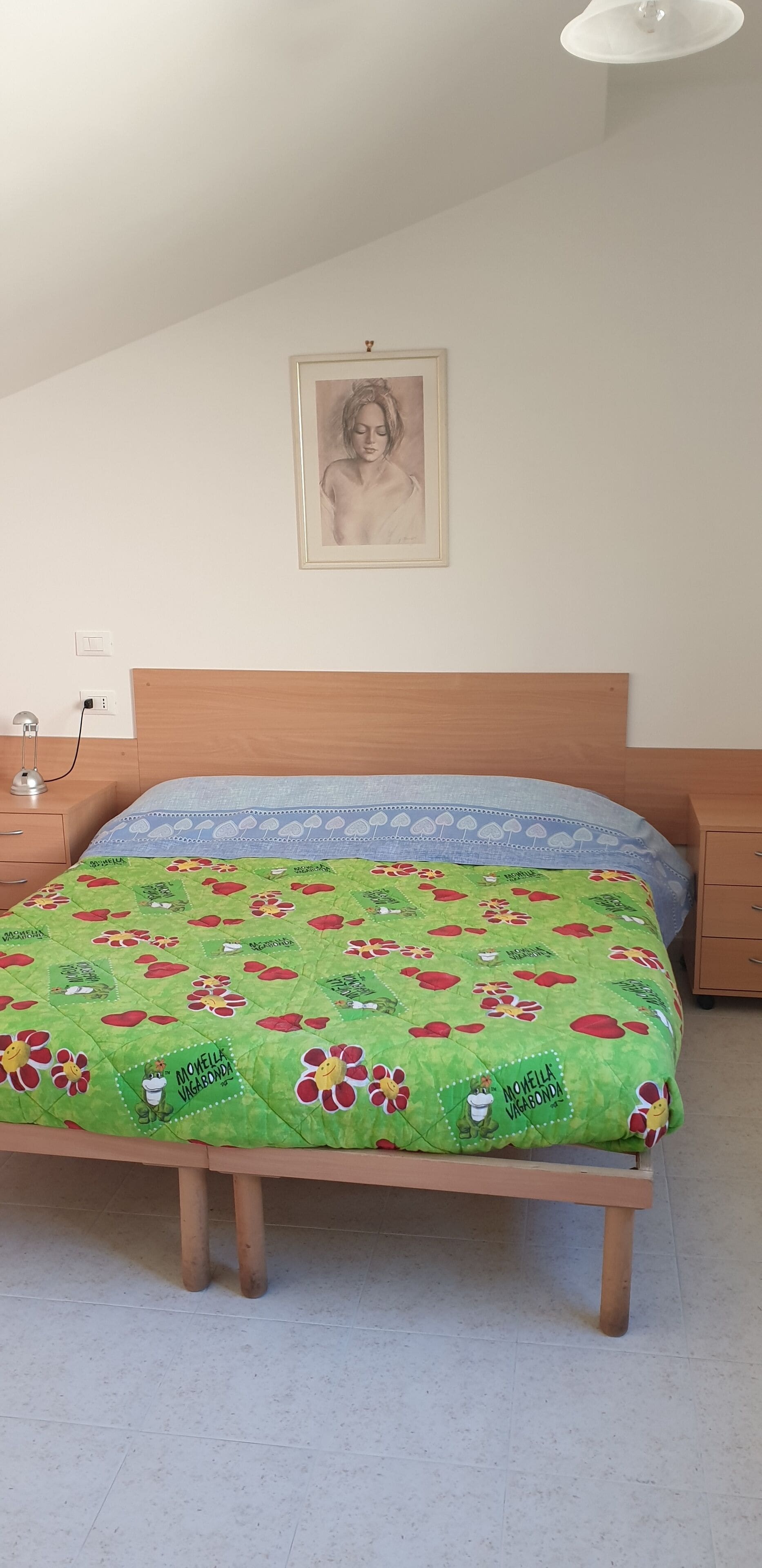 A bedroom with a bed, a nightstand, a lamp, and a framed picture on the wall.