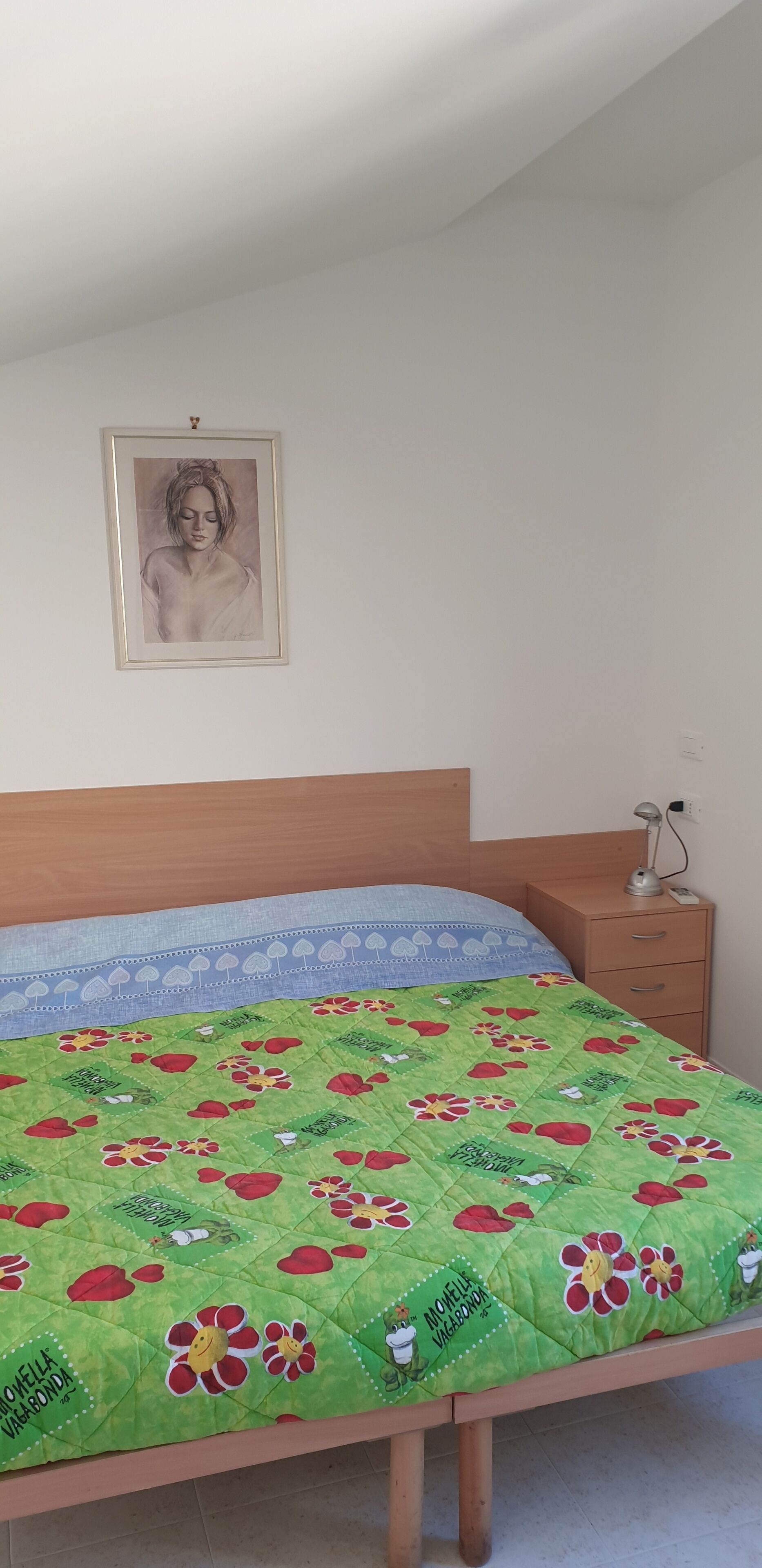 A bedroom with a bed, a nightstand, a lamp, and a framed picture on the wall.