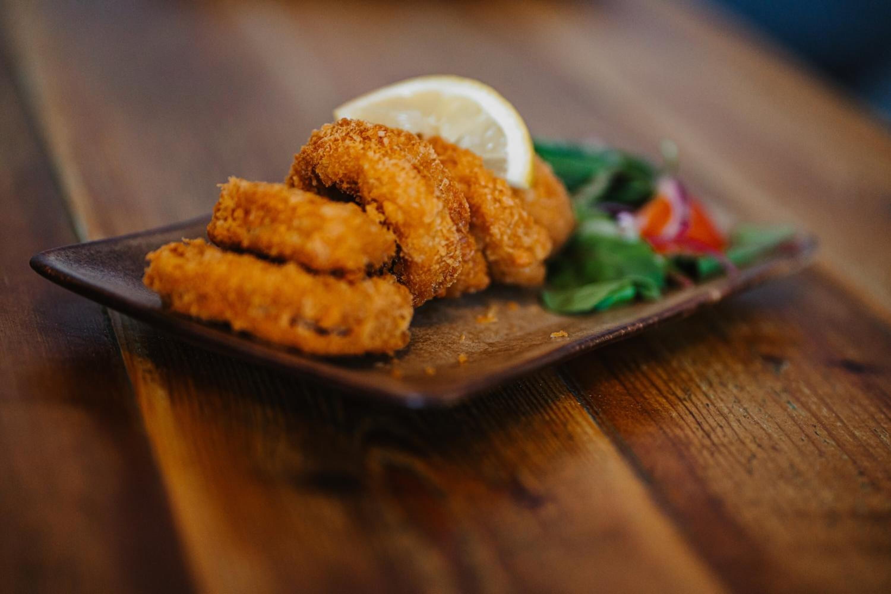 A plate of breaded and fried food items, possibly chicken tenders, served with a slice of lemon and a side salad.