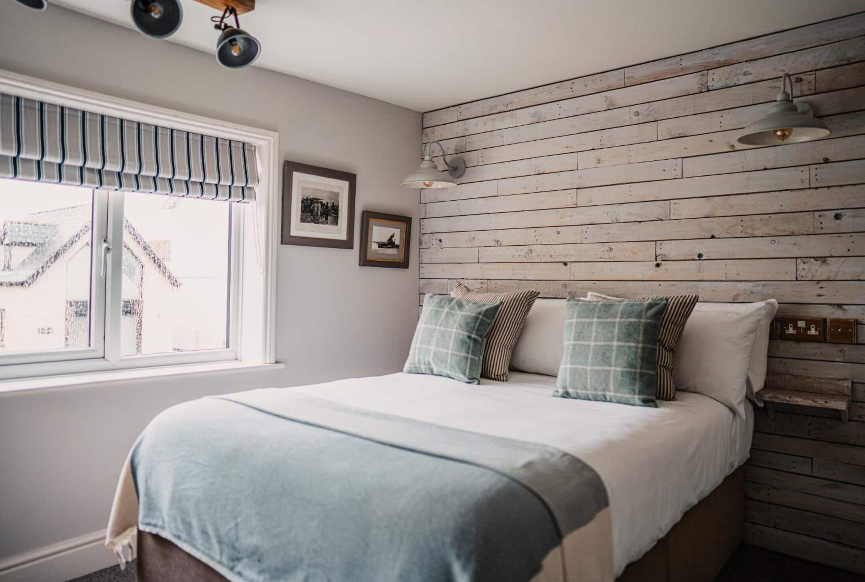 Un dormitorio con cama, ventana con vistas, pared de madera y una lámpara en el techo.