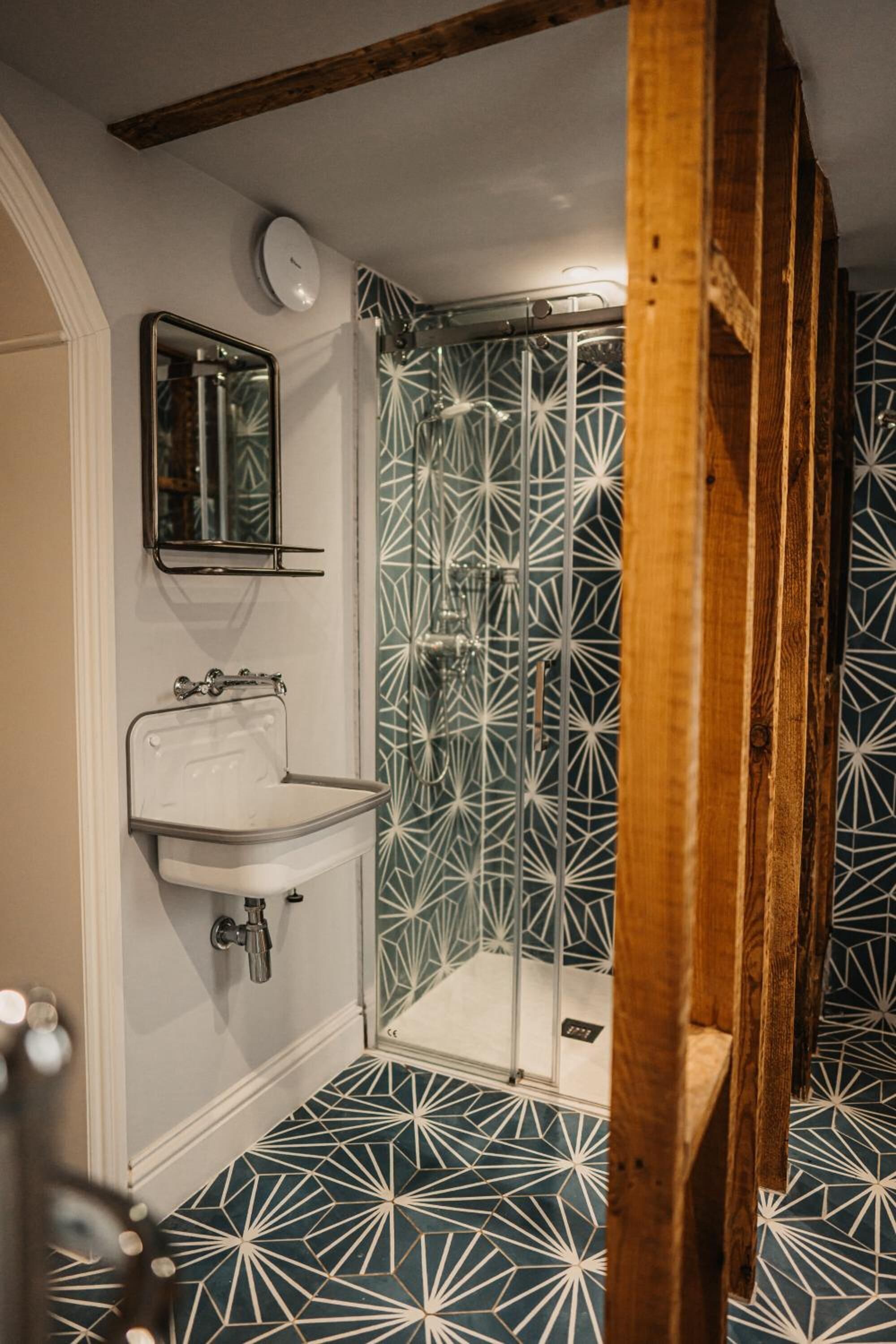 Un bagno con pavimento a motivi geometrici, un lavandino bianco con specchio sopra e zona doccia con porta in vetro.