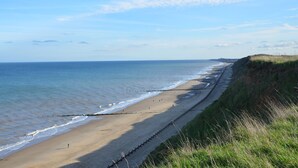 A beach with a long stretch of sand, a grassy cliff, and the ocean. - The Ship Inn (Norwich)